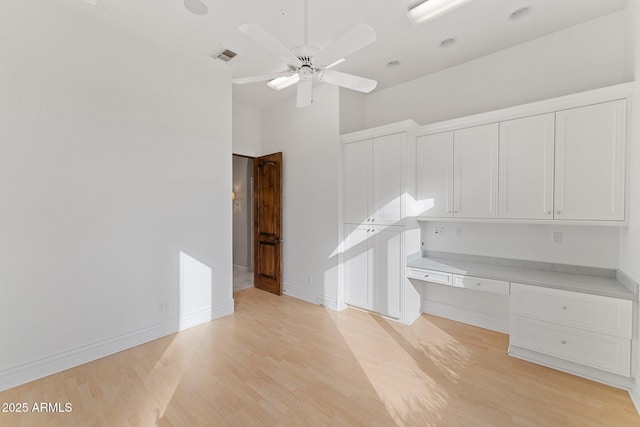 interior space with built in desk, ceiling fan, a towering ceiling, and light hardwood / wood-style floors