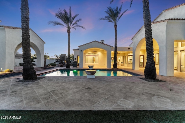 pool at dusk with ceiling fan and a patio