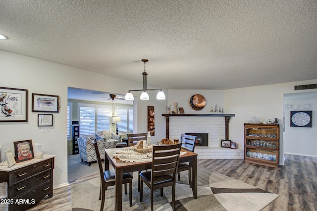 dining area featuring a textured ceiling, ceiling fan, a fireplace, and wood-type flooring