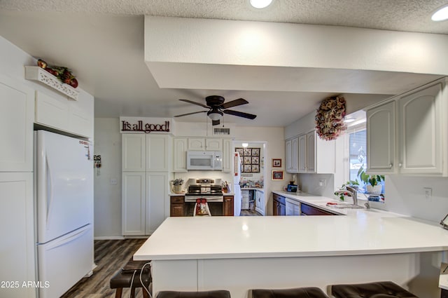 kitchen featuring white appliances, a kitchen breakfast bar, dark hardwood / wood-style floors, and kitchen peninsula