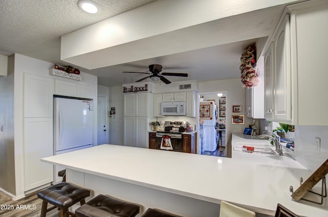 kitchen featuring white appliances, white cabinetry, a breakfast bar, and kitchen peninsula