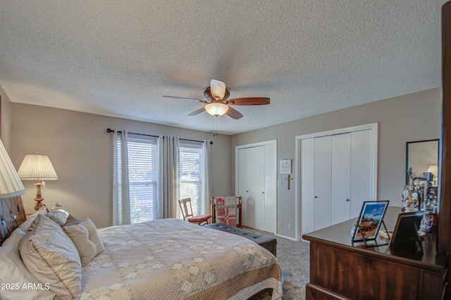 bedroom with ceiling fan, two closets, carpet, and a textured ceiling