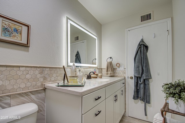 bathroom with toilet, vanity, and tile walls