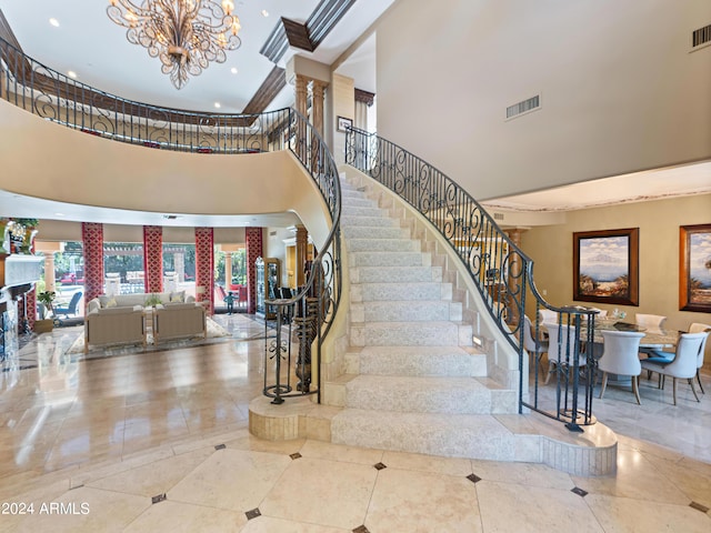 stairway featuring a towering ceiling, ornate columns, tile patterned floors, and a chandelier