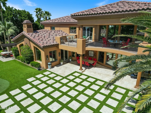 back of house featuring a patio, stucco siding, a lawn, a balcony, and a tiled roof