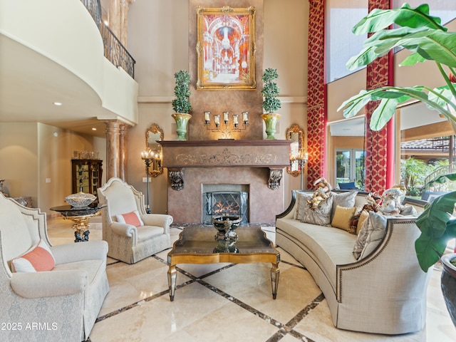 living area featuring a warm lit fireplace, a towering ceiling, and decorative columns