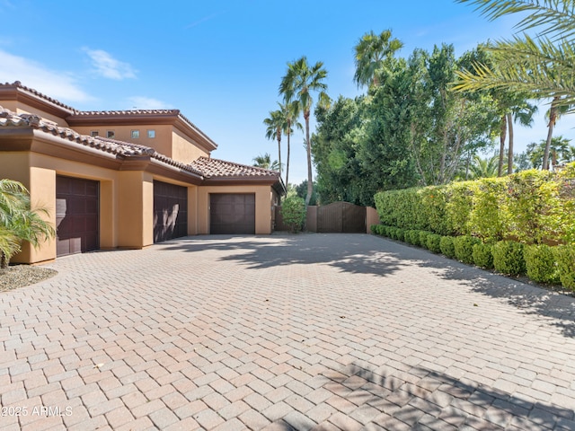 view of property exterior featuring decorative driveway, a tile roof, stucco siding, fence, and a garage