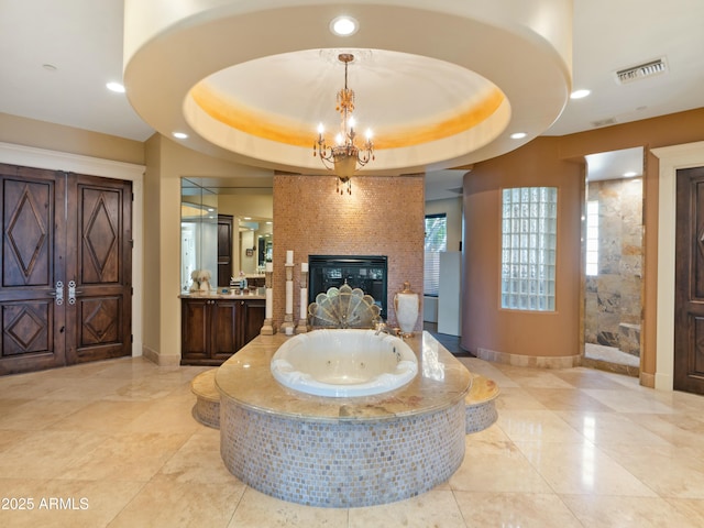 full bath featuring visible vents, a raised ceiling, a glass covered fireplace, vanity, and a notable chandelier