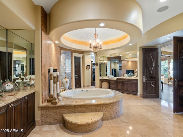 full bath featuring a tray ceiling, vanity, a bath, and a notable chandelier