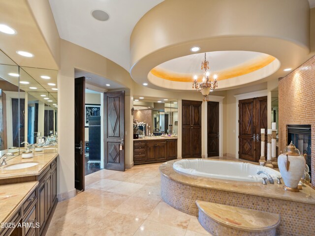 full bath featuring a glass covered fireplace, vanity, a bath, and an inviting chandelier