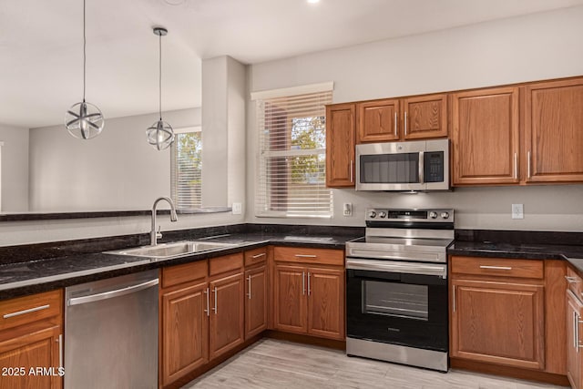 kitchen with appliances with stainless steel finishes, pendant lighting, sink, dark stone counters, and light wood-type flooring