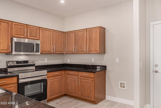 kitchen with dark stone countertops, light wood-type flooring, and appliances with stainless steel finishes