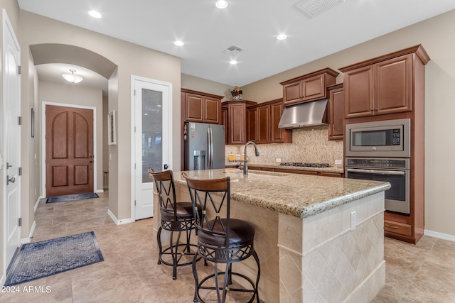 kitchen featuring backsplash, light tile patterned flooring, a center island with sink, and stainless steel appliances