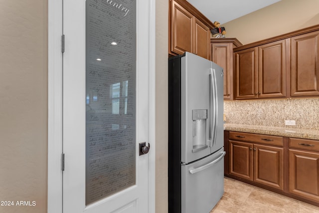 kitchen with light tile patterned floors, stainless steel refrigerator with ice dispenser, light stone counters, and backsplash