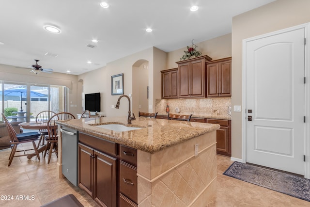 kitchen with a center island with sink, sink, light stone counters, backsplash, and dishwasher