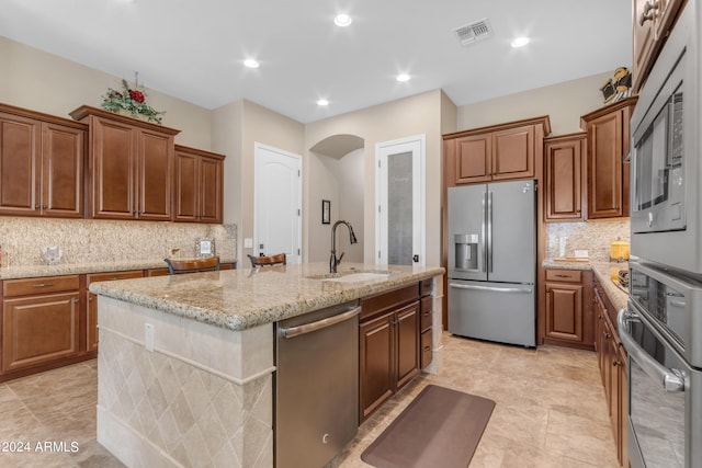 kitchen featuring light tile patterned floors, light stone counters, a kitchen island with sink, stainless steel appliances, and sink