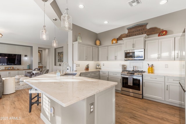 kitchen with pendant lighting, appliances with stainless steel finishes, a kitchen bar, and light hardwood / wood-style floors