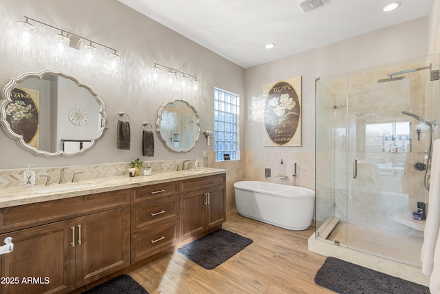 bathroom featuring wood-type flooring, plus walk in shower, tile walls, and vanity