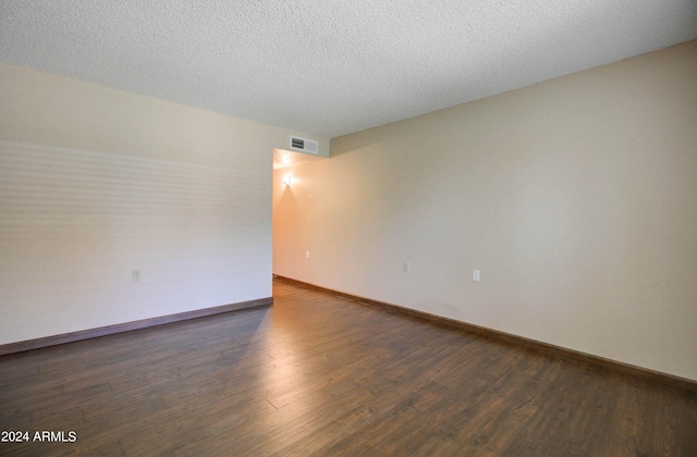 unfurnished room featuring dark wood-type flooring and a textured ceiling