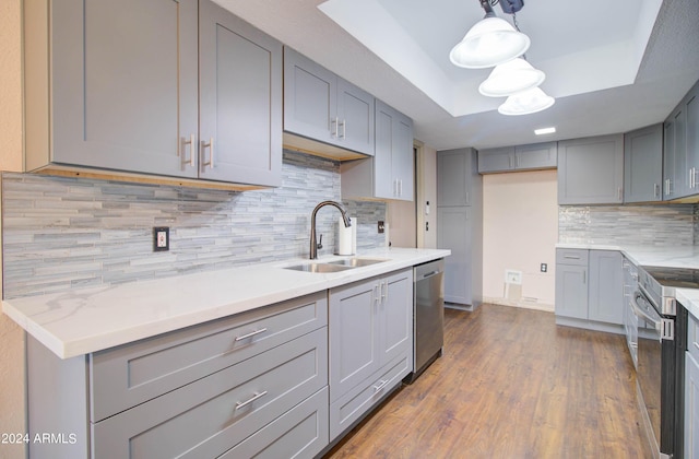 kitchen with appliances with stainless steel finishes, a tray ceiling, sink, and gray cabinetry