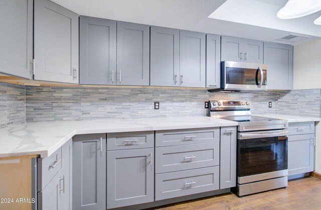 kitchen featuring decorative backsplash, light stone counters, appliances with stainless steel finishes, light hardwood / wood-style flooring, and gray cabinetry