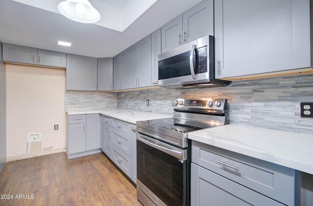 kitchen with stainless steel appliances, dark hardwood / wood-style flooring, light stone counters, backsplash, and gray cabinetry