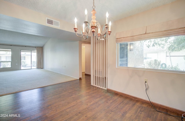 carpeted empty room featuring a textured ceiling, lofted ceiling, and a notable chandelier