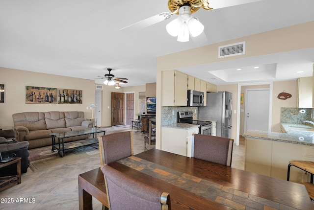 dining space with a raised ceiling, visible vents, and ceiling fan