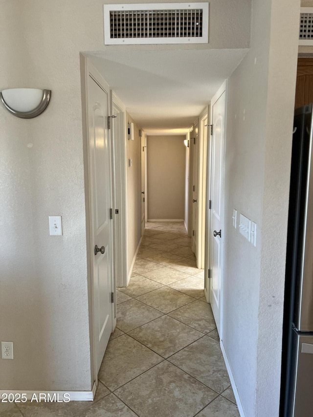 corridor featuring light tile patterned floors, baseboards, and visible vents