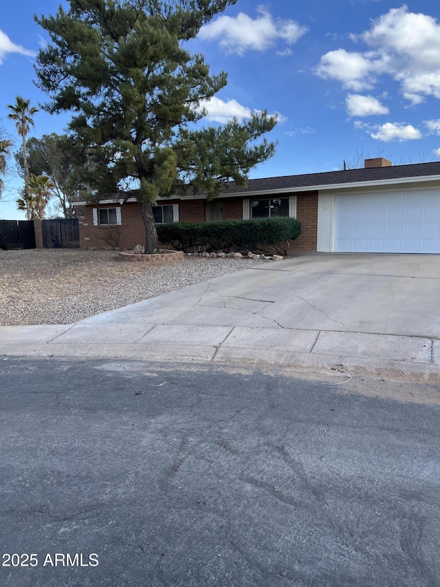 ranch-style home with concrete driveway, brick siding, an attached garage, and fence