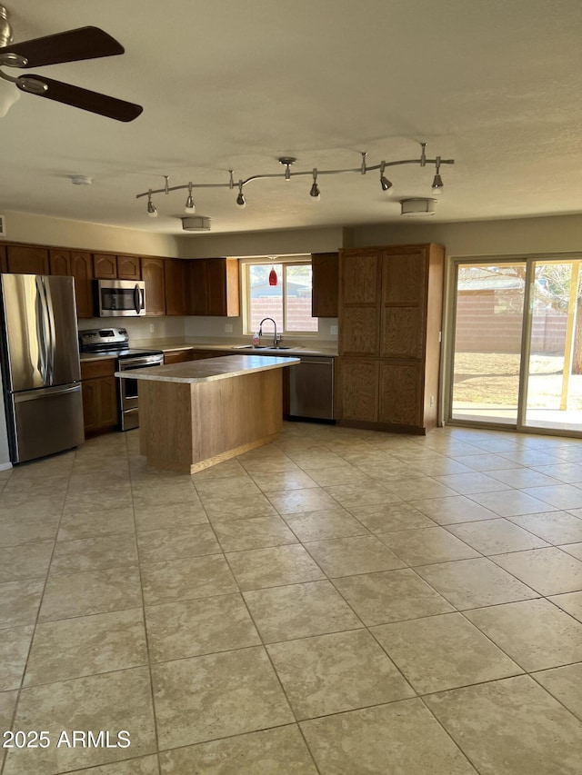 kitchen featuring ceiling fan, light tile patterned flooring, stainless steel appliances, a kitchen island, and a sink