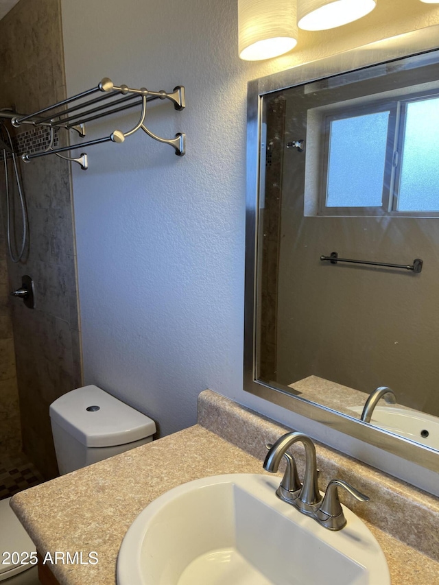 full bath featuring a textured wall, tiled shower, vanity, and toilet