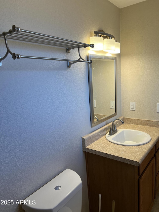 bathroom featuring toilet, a textured wall, and vanity