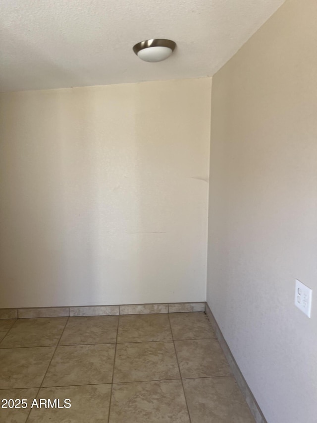 unfurnished room with light tile patterned floors, baseboards, and a textured ceiling