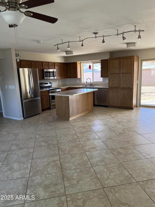 kitchen with stainless steel appliances, light countertops, light tile patterned flooring, a kitchen island, and a sink