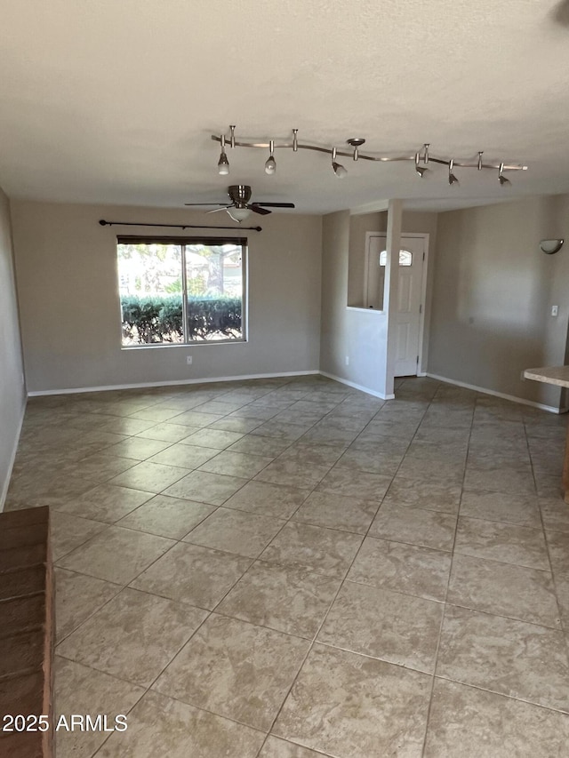 empty room featuring a ceiling fan, rail lighting, and baseboards