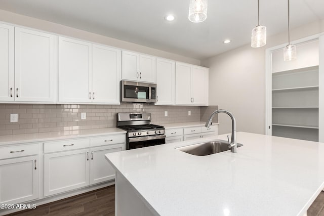 kitchen featuring a kitchen island with sink, hanging light fixtures, sink, appliances with stainless steel finishes, and white cabinetry