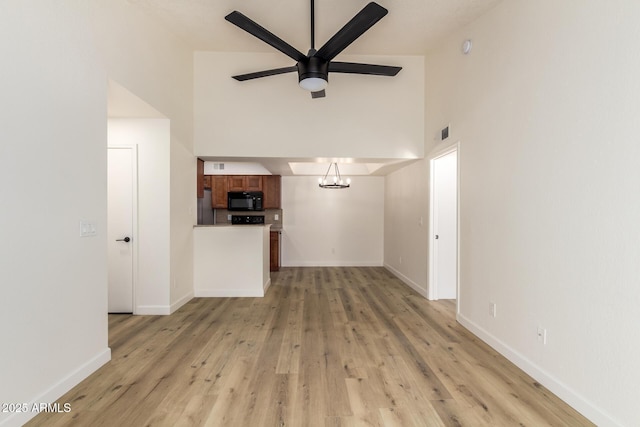 unfurnished living room with visible vents, baseboards, a towering ceiling, light wood-style flooring, and ceiling fan with notable chandelier