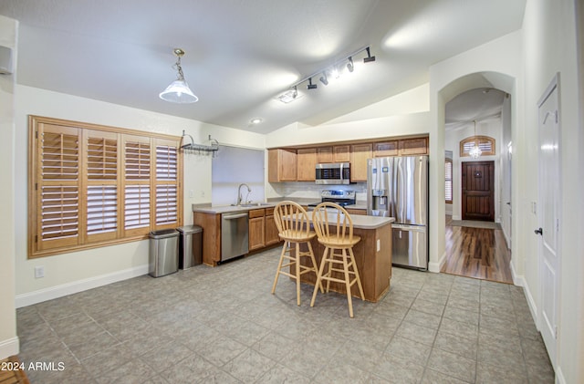 kitchen featuring appliances with stainless steel finishes, lofted ceiling, decorative light fixtures, sink, and a breakfast bar