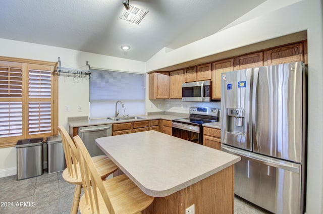 kitchen featuring stainless steel appliances, lofted ceiling, a kitchen island, a breakfast bar, and sink