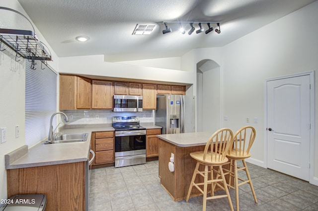 kitchen with backsplash, a kitchen island, a kitchen bar, sink, and appliances with stainless steel finishes