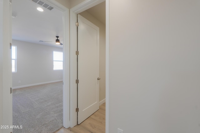 hallway featuring visible vents, light colored carpet, and baseboards