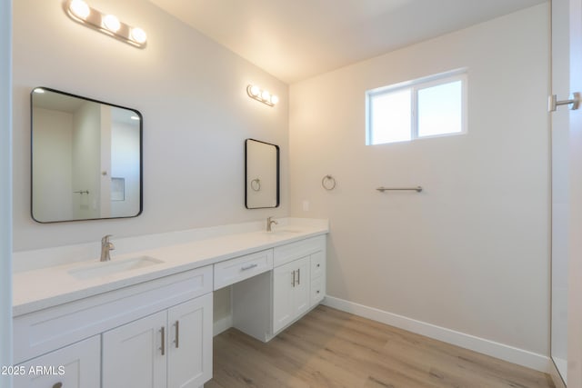 bathroom with double vanity, wood finished floors, a sink, and baseboards