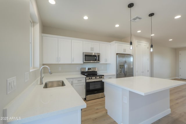 kitchen with white cabinets, appliances with stainless steel finishes, a center island, light wood-type flooring, and a sink