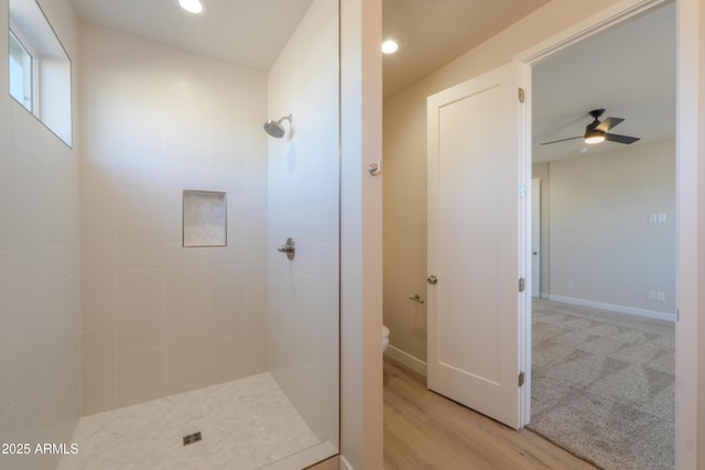 bathroom with toilet, a ceiling fan, a tile shower, wood finished floors, and baseboards