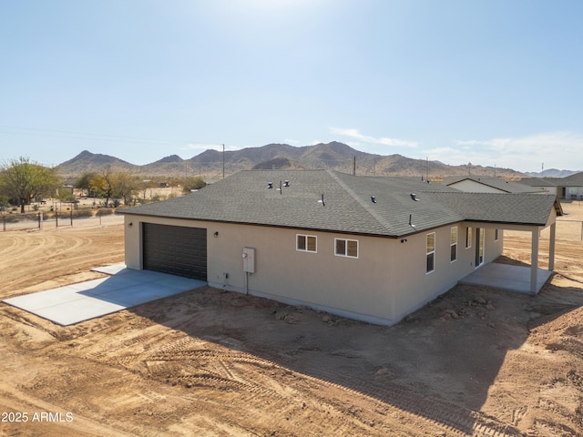 view of property exterior featuring a garage, concrete driveway, roof with shingles, a mountain view, and stucco siding