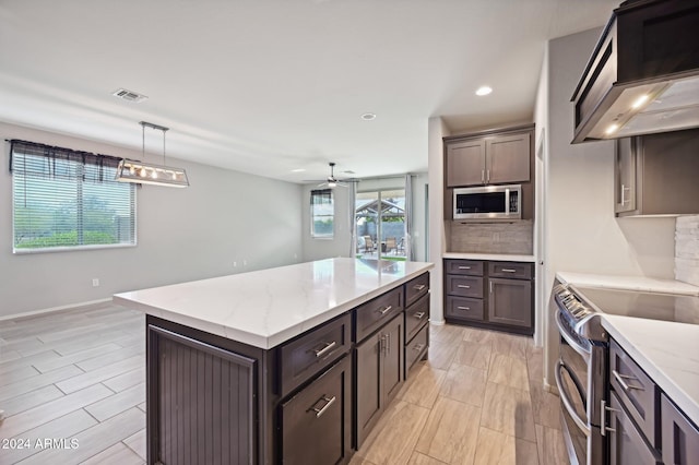 kitchen featuring hanging light fixtures, custom range hood, ceiling fan, a kitchen island, and appliances with stainless steel finishes