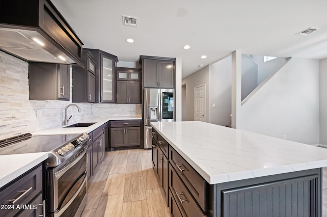 kitchen featuring stainless steel appliances, backsplash, custom range hood, sink, and a center island