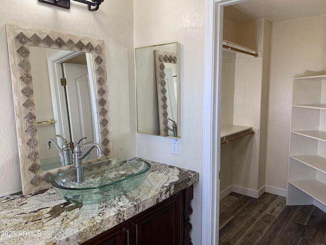 bathroom with a spacious closet, wood finished floors, vanity, and baseboards
