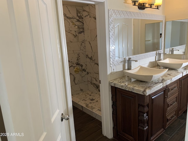 full bathroom with double vanity, tiled shower, a sink, and wood finished floors